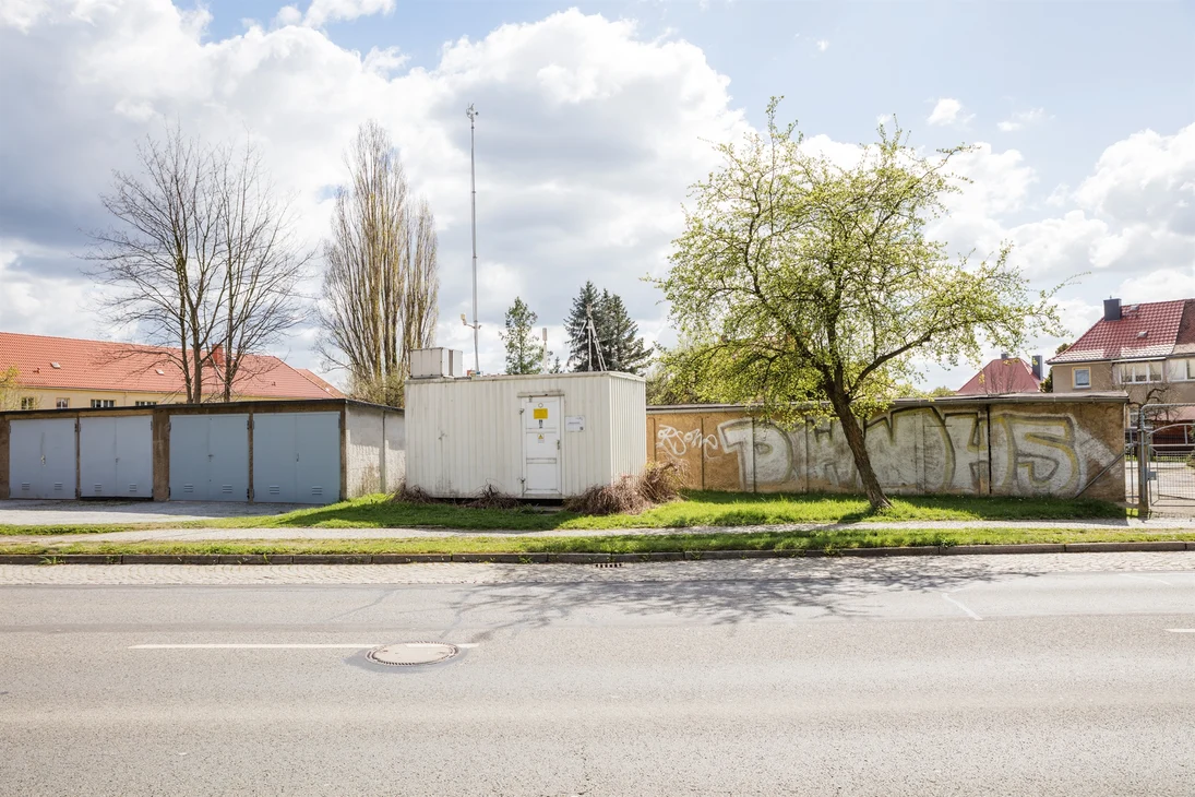 Die Messstation in Bautzen (weißer Container mit Probenahmeeinrichtungen auf dem Dach) befindet zurückgesetzt an einer Straße neben Garagen. Im Hintergrund sieht man Mehrfamilienhäuser.