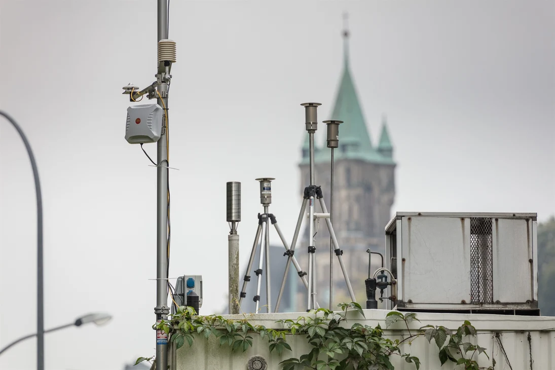 Das Bild zeigt das Dach der Messstation in Annaberg-Buchholz. Hinter den Probenahmen der Luftschadstoffe sieht man die Sankt-Katharinen-Kirche.en